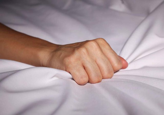 Women's fist clutching bed sheets in satisfaction after good sex